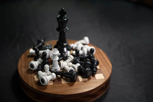 Tiny White king facing Black king in 5 times size. Both standing on a wooden chess board while others from both sides already dead. Only leader for a last fight. Local vs. Global. small vs. Giant.