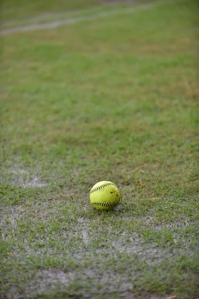 A fresh green softball left on a raining field waiting for a league match to begin while the field is full with water and no player.