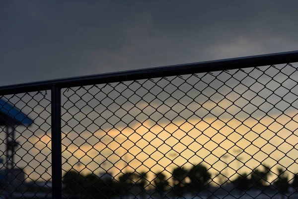 A close-up of a silhouette chain link fence in a sport field with a nice scene of a sun set as a background.