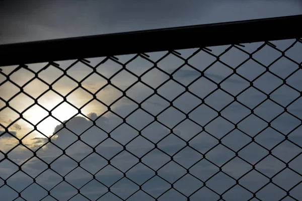 A close-up of a silhouette chain link fence  with a nice scene of a sun set as a background. 