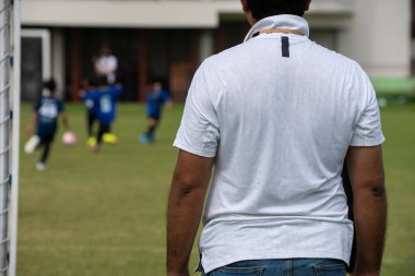 Baba, oğlunun güneşli bir günde bir okul turnuvasındaki futbol maçını seyrediyor. Spor, açık hava etkinliği, yaşam tarzı, mutlu aile ve futbol annesi ve futbolcu baba kavramı..