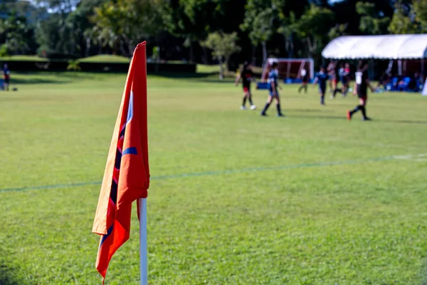 Orange corner flag from a football pitch, seeing group of players, coaches, staffs and parents getting together as a team in a background. Atmosphere from a youth football tournament in a summer time.