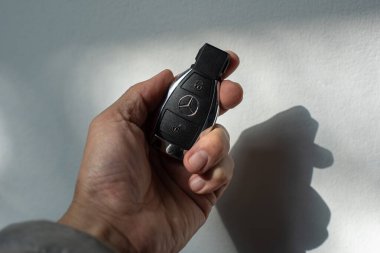 Bangkok, Tayland - 26 Ocak 2023 BENZ uzaktan kumandalı bir araba anahtarını güneşli bir günde beyaz bir arka planda tutan bir erkeğin yakın çekimi.