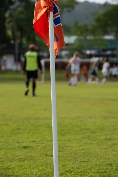 Orange corner flag from a football pitch, seeing group of players, coaches, staffs and parents getting together as a team in a background. Atmosphere from a youth football tournament in a summer time.