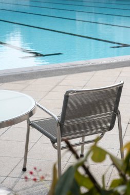 Rahatlatıcı bir atmosferi olan bir spor kulübünün havuzunun yanında oturacak birini bekleyen rahat bir sandalye ve yuvarlak cam masa. Tatiller, uzun tatiller ya da kısa tatiller.
