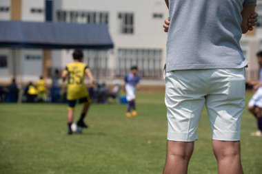 Futbol babaları açık havada ve güneşli bir günde oğlunun okul turnuvasında futbol oynamasını izliyor. Spor, açık hava etkinliği, yaşam tarzı, mutlu aile ve ev hanımı anne ve baba kavramı.