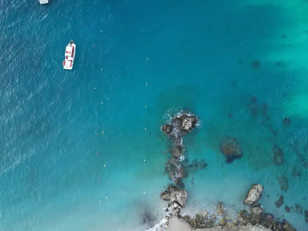 Turkuaz deniz suyundaki kayalıklı teknenin havadan çekilmiş fotoğrafı.