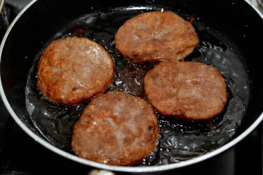 Kızartma tavasında kaynayan sığ bir yağda pişirilmiş 4 parça baharatlı sığır etli burger, fast food, abur cubur konsepti, ev yapımı fast food, seçici odaklanma.