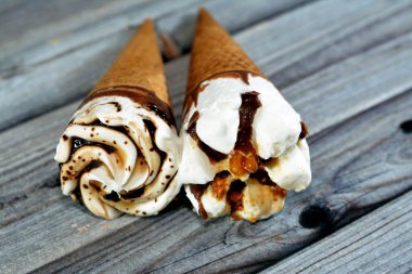 Çikolata ve karamel soslu vanilyalı dondurma külahları ve gevrek bir külahta fındıklar. Soğuk dondurmayı bisküvinin içinde eritmenin seçici odağı. Yaz tatili konsepti.