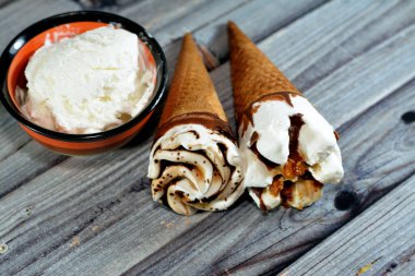 Çikolata ve karamel soslu dondurma külahları ve yanında vanilya kepçesi olan gevrek bir gofret külahında fındık, waffle bisküvisinde erimiş soğuk dondurma, yaz tatili konsepti.