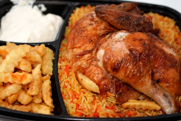 stock image Arabic Syrian cuisine of machine grilled barbecued chicken with colorful Basmati rice and French fries finger potatoes served in a black disposable plate served with garlic sauce, selective focus