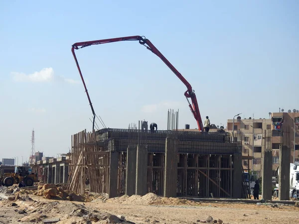 Kahire, Mısır, 7 Aralık 2022: Yolun kenarına kamyon monte edilmiş beton bir patlama pompası, yeni binanın inşaat alanındaki seçici odak noktası olan beton kamyona beton dökülüyor
