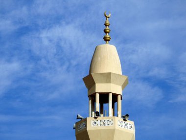 A high minaret of a mosque against a lovely blue sky with clouds at the daylight, Mosques are the place for worship and prayers for Muslims where they perform 5 Islamic prayers daily, selective focus