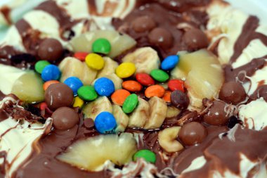 Chocolate mixture with biscuit and different types of chocolate pieces and cream with fresh pineapple ananas and bananas pieces on top on a dough baked and ready to be served, selective focus