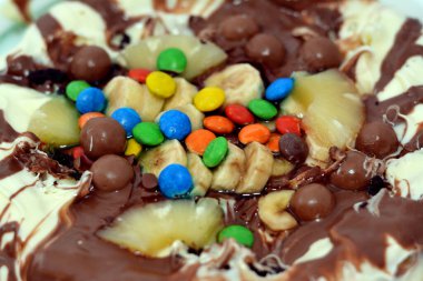 Chocolate mixture with biscuit and different types of chocolate pieces and cream with fresh pineapple ananas and bananas pieces on top on a dough baked and ready to be served, selective focus