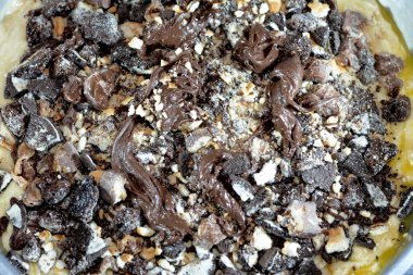baked dough covered with chocolate and stuffed with pieces of chocolate, biscuit, cake, caramel and brownies, ready to be cooked in the oven, selective focus of a chocolate sweet pastry cake