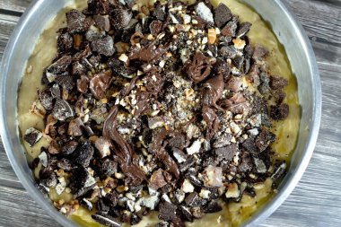 baked dough covered with chocolate and stuffed with pieces of chocolate, biscuit, cake, caramel and brownies, ready to be cooked in the oven, selective focus of a chocolate sweet pastry cake