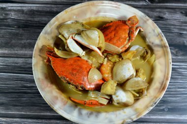 Hot soup meal of various fresh seafood marine crabs, shrimps, clams, mussels, gandofli, oysters, crab sticks, calamari, squid and fish fillet cooked on hot steam merged in water, milk, lime and spices