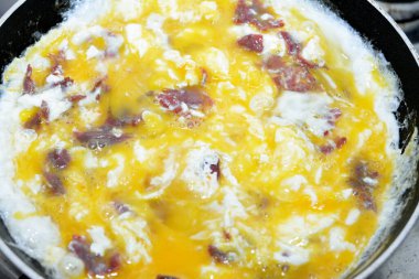 Scrambled eggs with pastrami, a dish made from eggs stirred, whipped or beaten together while being gently heated, with salt, butter, oil and black pepper with slices and pieces of beef pastrami