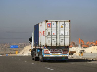 Giza, Egypt, January 26 2023: flatbed truck big vehicle with a steel shipment container on it on a highway in Egypt, shipment and delivery service concept, lorry transfer container, selective focus
