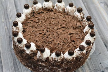 Krem şanti ve çikolatayla doldurulmuş çikolatalı pasta, üzerinde parçalanmış kahverengi çikolata katmanları ve üzerinde çikolatalı gevrek toplarla beyaz vanilyalı krema.