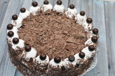 Krem şanti ve çikolatayla doldurulmuş çikolatalı pasta, üzerinde parçalanmış kahverengi çikolata katmanları ve üzerinde çikolatalı gevrek toplarla beyaz vanilyalı krema.