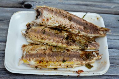 Buğday taneli ızgara tekir balıklarının seçici odak noktası, tek kullanımlık beyaz tabakta temizlenip servis edilmesi, ızgara Mısırlı tekir balığının deniz ürünleri mutfağı, ahşap zeminde izole edilmiş lezzetli yiyecekler.