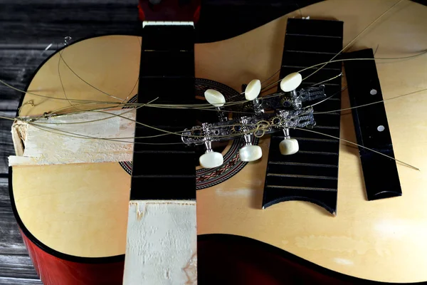 A broken wooden old classic guitar with damaged strings chords, shattered musical instrument, unattached damaged guitar with cut chord and wood, selective focus of non working music instrument