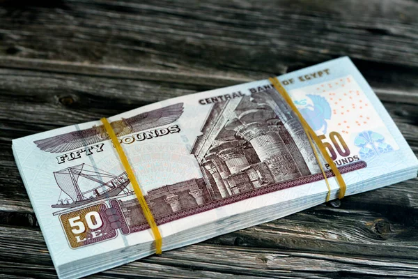 Egypt money stack of pounds isolated on wood background, pile of 50 EGP LE fifty Egyptian pounds cash money bills with a image of Abu Hurayba Mosque, temple of Edfu and winged scarab, selective focus