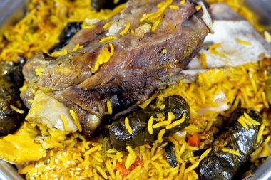 A well cooked lamb shank with yellow Basmati rice and mixed vegetables and stuffed grape leaves mahshi Mahshy with white rice cooked roasted in the oven slowly in a pottery casserole, selective focus clipart