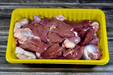 Çiğ tavuk ciğeri, bağırsaklar ve kalpler taze ciğerin seçici odağı, taşlık ve protein dolu tavukların kalbi ahşap arka planda izole edilmiş, pişirilmeye hazır, tek kullanımlık sarı bir tabakta.