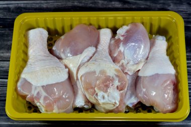 Taze çiğ tavuk butları, pişmeye, ızgaraya, ızgaraya, ızgaraya, kızarmaya ya da kaynatmaya hazır deri ve kemiklerle arka tarafta. Sarı tabakta tavuk budu beyaz etinden seçici bir odak noktası.