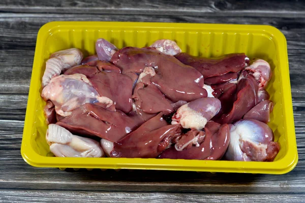 Raw chicken livers, gizzards and hearts, selective focus of fresh liver, gizzard and heart of chickens full of protein in a yellow disposable plate isolated on wooden background ready to be cooked