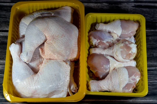 uncooked fresh raw chicken legs drumsticks and thighs hindquarter leg quarters with skin and bones in a yellow disposable plate isolated, ready for baking, grilling, barbecuing, frying or boiling