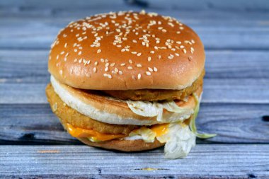 Ekmek arası tavuk köftesi, kıtır marul, eritme peyniri, soğan, turşu ve kızarmış susamlı çöreğin arasına çerçevelenmiş sosun lezzetli bir kombinasyonu. Çift tavuklu sandviç, seçici odaklanma.