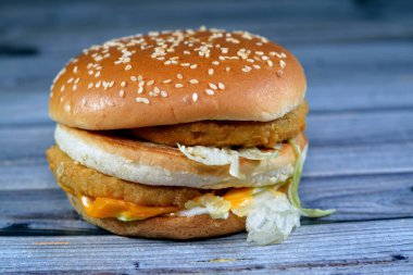 Ekmek arası tavuk köftesi, kıtır marul, eritme peyniri, soğan, turşu ve kızarmış susamlı çöreğin arasına çerçevelenmiş sosun lezzetli bir kombinasyonu. Çift tavuklu sandviç, seçici odaklanma.