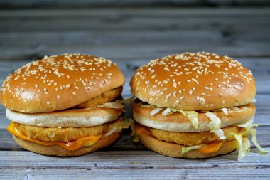 Ekmek arası tavuk köftesi, kıtır marul, eritme peyniri, soğan, turşu ve kızarmış susamlı çöreğin arasına çerçevelenmiş sosun lezzetli bir kombinasyonu. Çift tavuklu sandviç, seçici odaklanma.