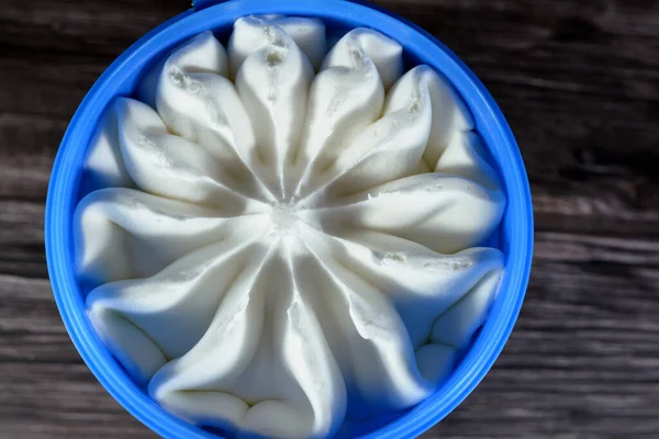 木製の背景に隔離されたプラスチック製のボウルにバニラホワイト冷凍アイスクリームを提供する準備ができて 青い容器の花の形をしたバニラアイス 選択的な焦点 — ストック写真