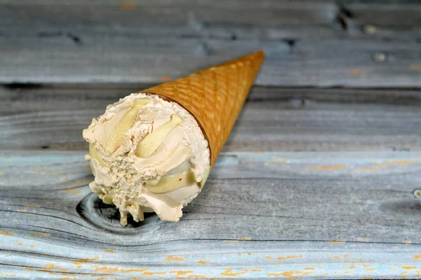クリスピーなウェーハコーンの中の特別な味のアイスクリーム 木製の背景 夏と休日のコンセプト 選択的な焦点に隔離されたウェーハビスケットで冷たいアイスクリームの小枝を溶かす — ストック写真