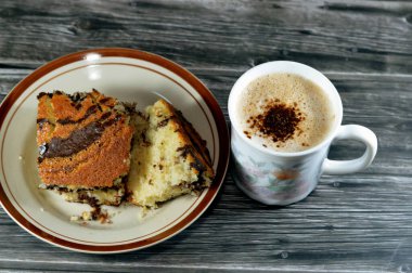 Kremalı köpüklü ve kahveli bir kapuçino geleneksel olarak süt köpüğüyle hazırlanmış espresso bazlı bir kahve içeceği ve bir parça kaplan mermer sünger keki, tatlı sünger keki.