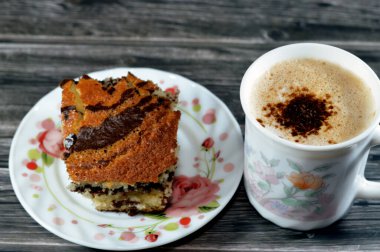 Kremalı köpüklü ve kahveli bir kapuçino geleneksel olarak süt köpüğüyle hazırlanmış espresso bazlı bir kahve içeceği ve bir parça kaplan mermer sünger keki, tatlı sünger keki.