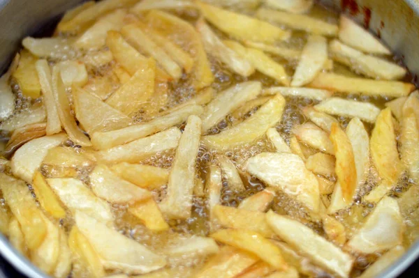 Close-up of French fries potatoes frying in boiling hot oil in a deep fryer at home. French fries, Junk food concept, home made deep fried chips, selective focus