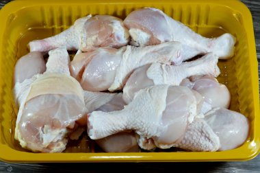 Taze çiğ tavuk butları, pişmeye, ızgaraya, ızgaraya, ızgaraya, kızarmaya ya da kaynatmaya hazır deri ve kemiklerle arka tarafta. Sarı tabakta tavuk budu beyaz etinden seçici bir odak noktası.