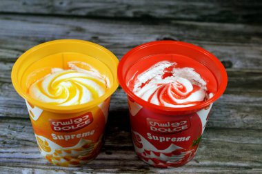 Kahire, Mısır, 6 Temmuz 2023: Dolce Supreme dondurması mango ya da çilek sosu gibi meyve soslu dondurulmuş vanilya, DOLCE dondurmalı Mısır ürünleri ahşap arka planda izole edilmiş tatlar
