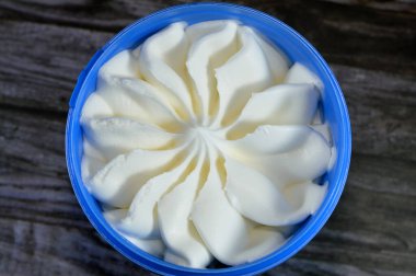 Tahta arka planda izole edilmiş plastik bir kasede dondurulmuş vanilyalı dondurma servis edilmeye hazır mavi kapta çiçek şeklinde vanilyalı dondurma seçici bir odak noktası.