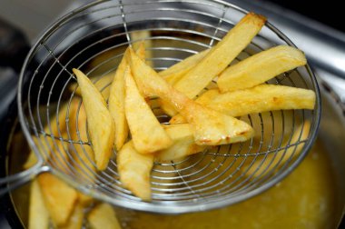 Evdeki fritözde kızgın yağda kızartılmış patates kızartması yakın. Patates kızartması, abur cubur konsepti, ev yapımı kızarmış cips, seçici odaklanma.