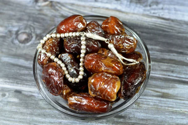 Ramadan background, Ajwa dates, a cultivar of the palm date that is widely grown in Medina, Saudi Arabia., an oval-shaped, medium-sized date, and an Islamic silver rosary in silver color with 33 beads