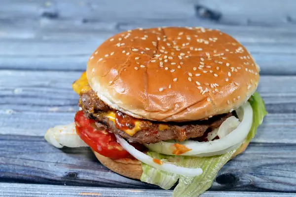 A juicy thick double beef patty with cheese covered with sauce, crispy lettuce, fresh tomatoes, onions and pickles in a large sesame seed bun, a beef burger hamburger sandwich with special sauces