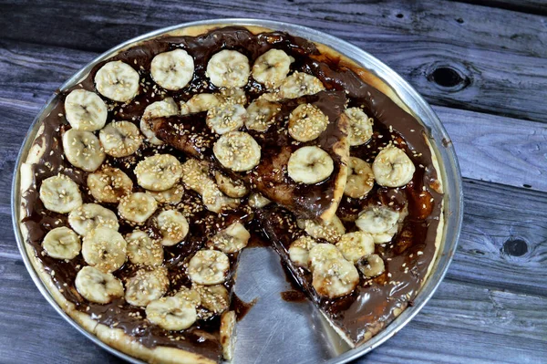 A sweet baked pastry of chocolate pizza that baked in the oven then covered with melting chocolate and topped with slices of fresh banana fruit and sesame seeds, a chocolate pie sweet dessert