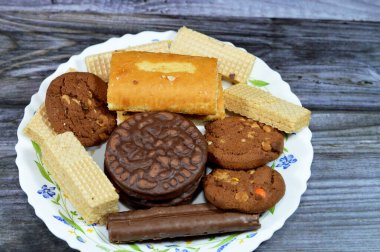 Çikolata çubuklu bir şeker tabağı, çikolata kremalı çıtır gofretler vanilyalı gevrek bisküviler, çilekli kremalı İsviçre dürümü, çikolatalı kurabiyeler.